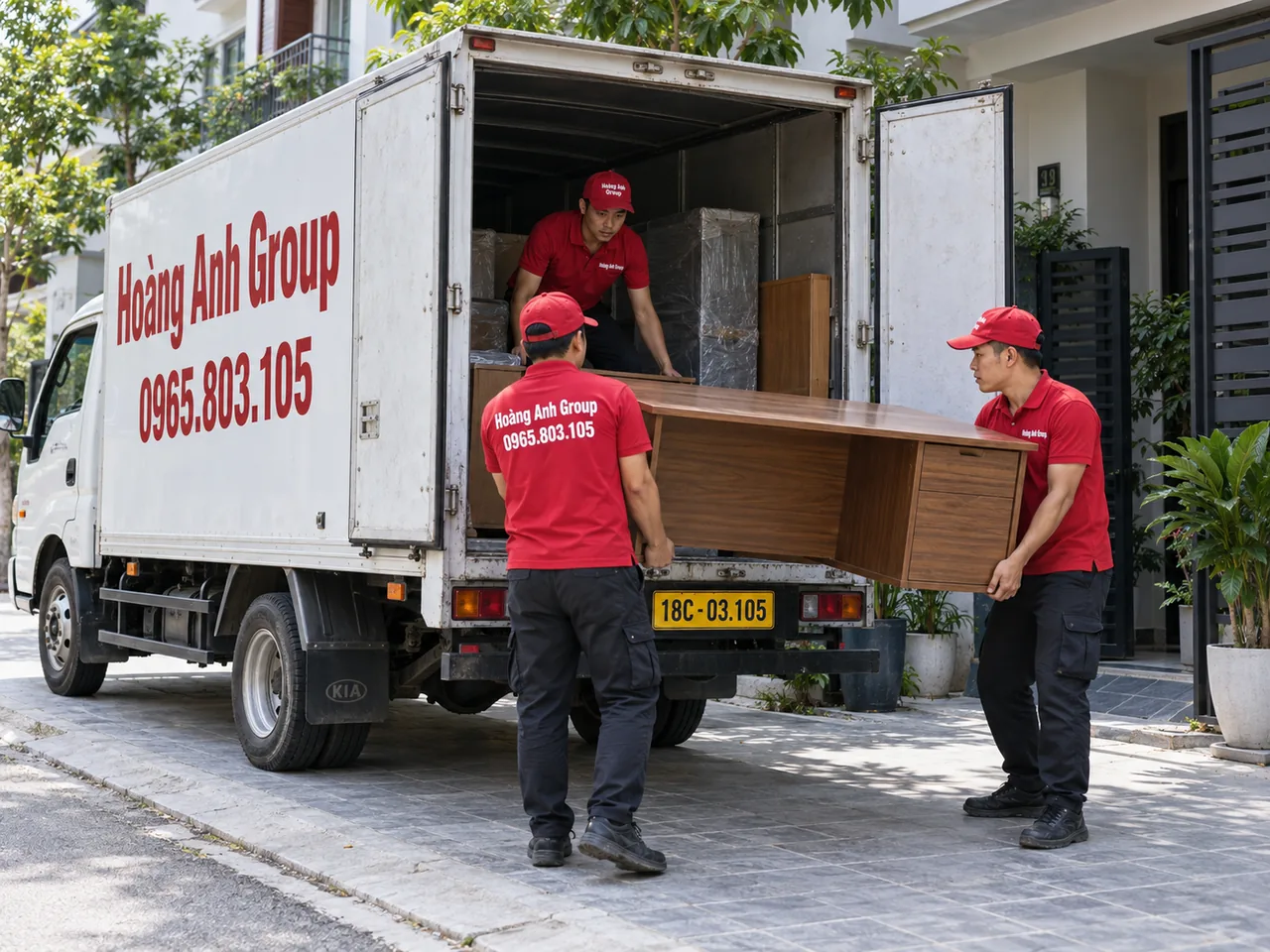 Hai nhân viên khiêng bàn gỗ về phía xe tải thùng kín, một nhân viên ở trong thùng xe