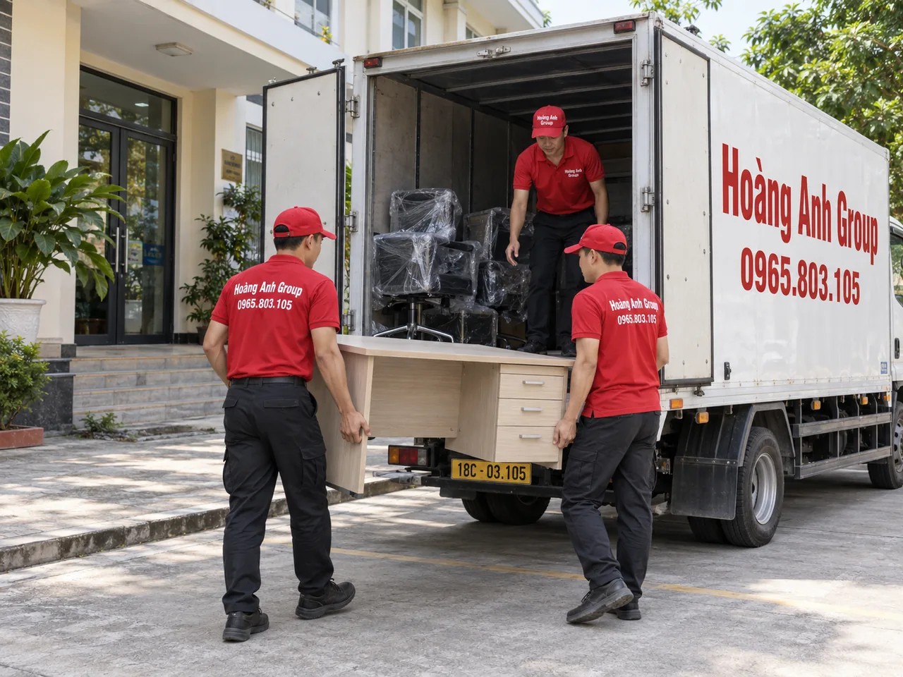 Hai nhân viên chuyển bàn văn phòng tới xe tải thùng kín, một nhân viên trong thùng xe